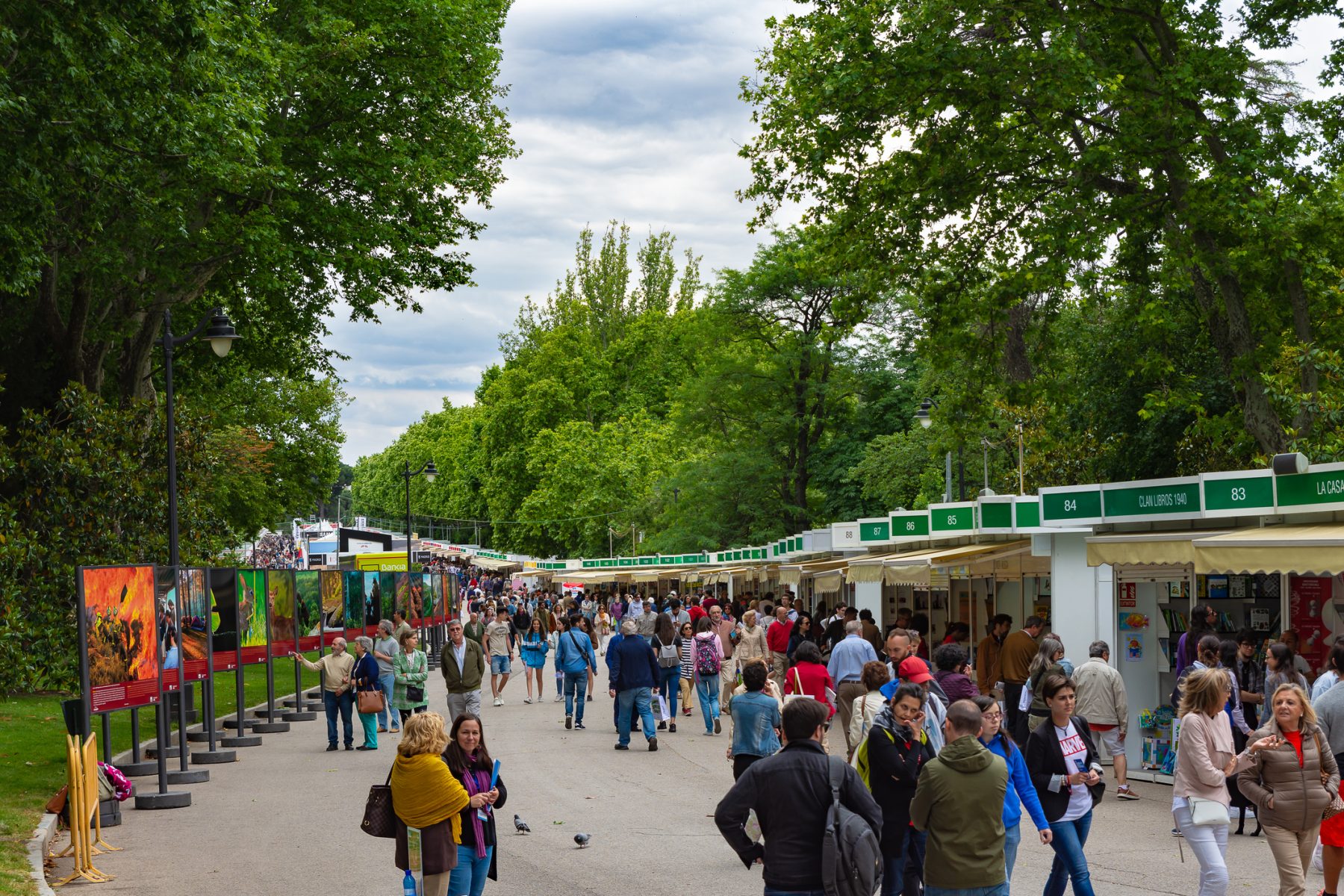 Visitantes recorriendo las casetas y una exposición fotográfica en la Feria del Libro de 2019